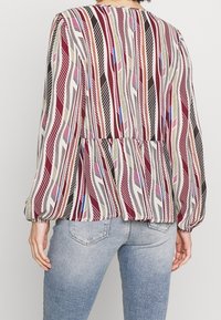 Langærmet bluse med et flerfarvet fjerdesign på en lys baggrund, med en samlet talje og elastiske manchetter.