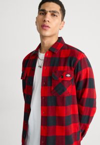 Rød og sort ternet flannel skjorte, bomuldsstof, knaplukning foran, to brystlommer, tekstureret finish, casual design.