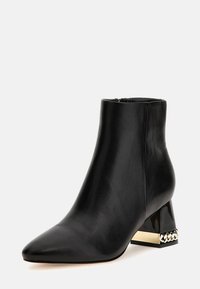 Stivaletto in pelle nera con punta affilata e tacco a blocco lucido nero, caratterizzato da un dettaglio a catena con accenti dorati alla base.