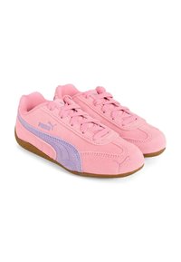 Un paio di sneaker Puma in suede rosa con striscia laterale viola e suole in gomma marrone, viste da un'angolazione laterale su sfondo bianco.