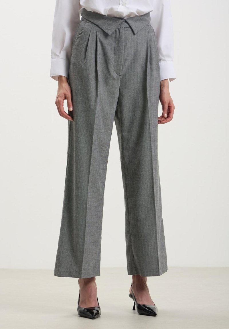 Pantaloni grigi a vita alta con finitura testurizzata, pieghe sulla parte anteriore e gambe larghe. Abbinati a décolleté nere a punta.