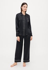 Black satin pajama set featuring a button-up shirt with a collar, white piping, and matching wide-leg pants. Includes a chest pocket.