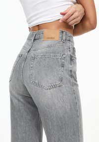 Blugi din denim gri cu talie medie, două buzunare la spate și o etichetă din piele bej la talie pe care este embosat "PULL&BEAR".