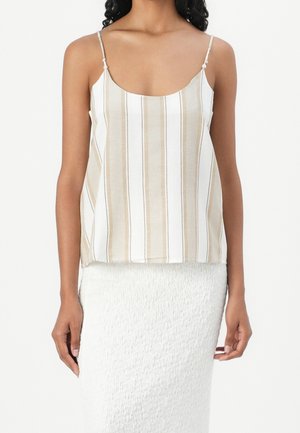 Kobieta ubrana w beżowo-biały top na ramiączkach z cienkimi paskami oraz białą teksturowaną spódnicę, na jednolitym tle.