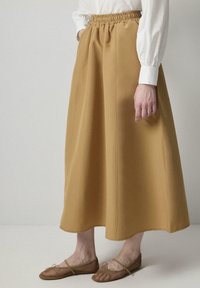 Una falda mostaza de longitud media con una cintura elástica, que presenta costuras verticales y una tela suave y texturizada. Combinada con unos bailes color beige.