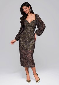 Figurbetontes Kleid mit tiefem Ausschnitt, langen Puffärmeln, schwarzem Blumenmuster auf einem dunkeloliven Hintergrund, knielang. Goldene Absätze.