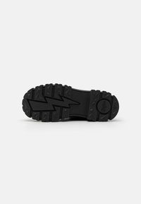Suela de zapato de goma negra con un patrón de tracción agresivo y diseño en zigzag, que presenta elementos triangulares y redondeados elevados para mejorar la tracción.