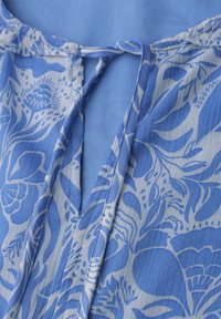 Tissu à motif floral bleu et blanc avec un décolleté en V et une fermeture par lien noué au col.