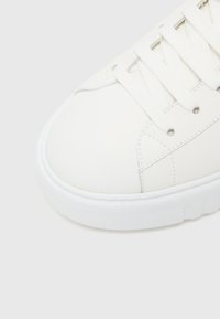 White sneaker with a smooth leather upper, round toe, classic lacing, textured detailing on the side, and a rubber sole.