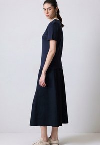 Mørkeblå bomulds t-shirt parret med en lang, svajende mørkeblå nederdel. Modellen bærer lyse sneakers, som fremviser et simpelt design og en strømlinet silhuet.