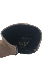Stivale alla caviglia in suede marrone con una texture morbida, dotato di un interno nero e di un logo sulla soletta. La cerniera è posizionata sul lato esterno.