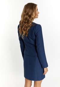 Abito blu navy a trama con maniche lunghe, caratterizzato da una silhouette aderente e un delicato motivo a diamante. La vista posteriore mostra il tessuto liscio e un design semplice.