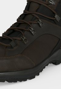 Κοντινή λήψη καφέ δερμάτινης πεζοπορικής μπότες με ανθεκτική μαύρη σόλα και μεταλλικά άγκιστρα που ασφαλίζουν σκούρα καφέ κορδόνια.