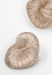 Oggetti decorativi metallici con un design testurizzato e vorticoso in un colore rosa oro chiaro, caratterizzati da scanalature e forme organiche.