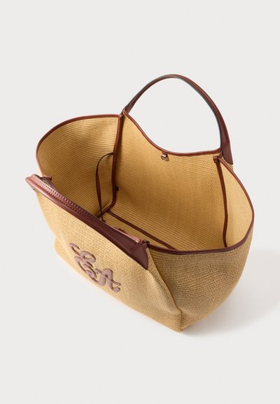 Μεγάλη μπεζ υφαντή τσάντα ώμου με καφέ δερμάτινη επένδυση και λαβές, ανοιχτό πάνω μέρος και λογότυπο "Coast" στο πλάι, εμφανίζεται άδεια με φόντο λευκό.