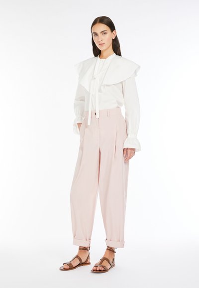 Camicia bianca con colletto arricciato oversize e dettaglio a fiocco, abbinata a pantaloni rosa pallido a vita alta e sandali marroni con cinturini.