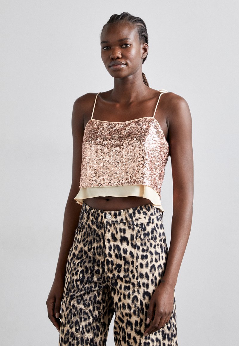 Top court en sequins rose doré, avec des bretelles fines et un ourlet volanté ; associé à un pantalon large en imprimé léopard avec des accents dorés.