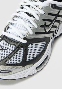 Nike sportbačiai su tinkliniu viršumi baltos ir juodos spalvų, su atspindinčiais sidabriniais akcentais, plokščiomis baltomis raištelėmis ir paminkštintu apykakle patogumui.