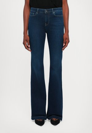 Jeans em flared azul escuro feitos de denim, com um design clássico de cinco bolsos e detalhes de costura discretos, combinados com sapatos pretos de bico fino.