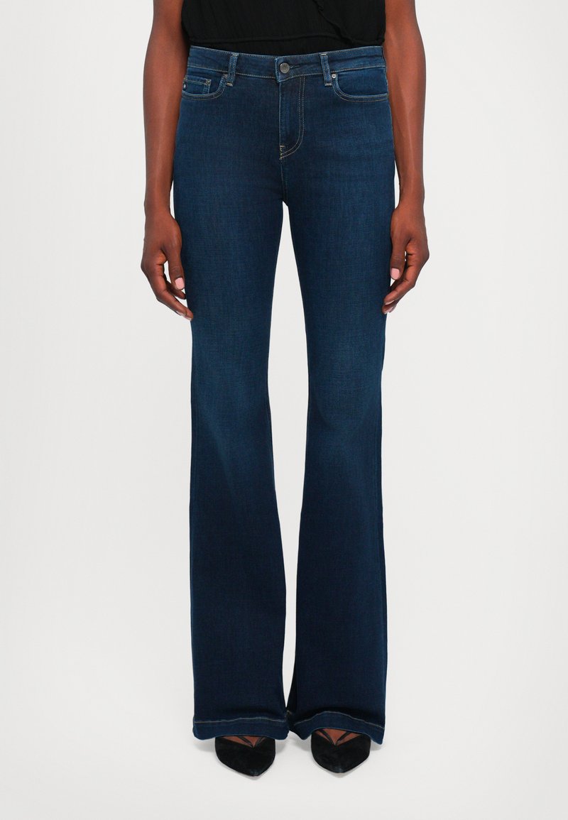 Mörkblå utsvängda jeans i denim med klassisk femficksdesign och subtila sömnadsdetaljer, i kombination med svarta spetsiga skor.