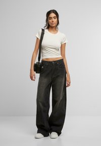 Svart vide jeans med en litt falmet finish, kombinert med en tettsittende hvit T-skjorte med korte ermer. En liten svart kameraveske henger fra skulderen.