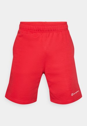 Shorts de sport rouges en tissu lisse, avec une ceinture élastique et un petit logo en accent sur le côté inférieur.