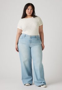 Light-colored, wide-leg jeans with a slightly faded texture, paired with a cream short-sleeved shirt. The outfit has a relaxed fit.