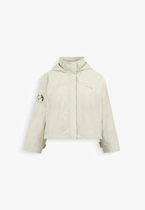 Lichtbeige capuchonjack met hoge kraag, lange mouwen en subtiele logo's op de borst en linkerarm, weergegeven op een witte achtergrond.