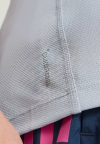 Kratki kadar svijetlosive teksturirane tkanine s logotipom "Climacool" i vidljivim šavovima, u paru s tamnim kratkim hlačama sa ružičastim prugama.