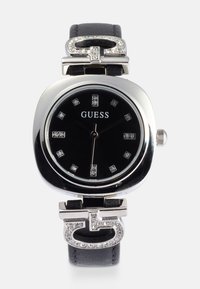 Zwarte leren strap uurwerk met een vierkante zilverkleurige behuizing, zwarte wijzerplaat, kristallen uurmarkeringen en een logo-accent met rhinestones.