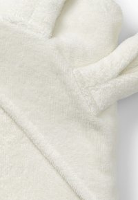 Kermanvärinen kädenlämmittimet, jotka on valmistettu pehmeästä, pörröisestä materiaalista. Niissä on pyöristetyt sormet ja tekstuuri, joka lisää mukavuutta.