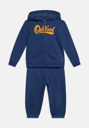 Marineblaue Kapuzenjacke für Kleinkinder mit gelbem "OshKosh" Text und passenden blauen elastischen Bundhosen.