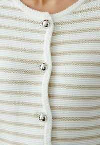 Lightweight knitted cardigan in white with beige horizontal stripes, featuring a rounded neckline and shiny silver buttons.