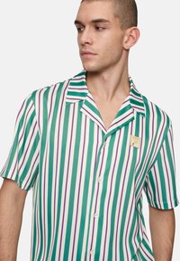 Korte mouw shirt met verticale strepen in groen, wit en paars. Klassieke kraag, knopenlijst en een merkembleem op de borst.