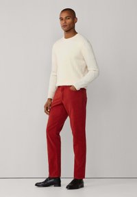 Pantalones de algodón rojos combinados con un suéter blanco de punto con trenzas. El look se complementa con zapatos de vestir negros. Diseño simple y ajustado.