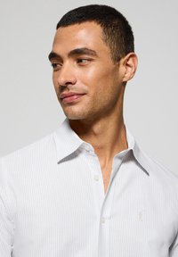 Camicia a righe grigio chiaro con colletto, caratterizzata da una leggera trama e un piccolo logo ricamato sul lato sinistro del petto.