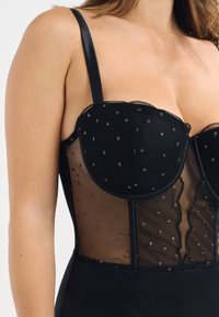 Bodysuit noir avec des panneaux en maille transparente, parsemé d'accents cuivrés. Il possède des bonnets moulés et des larges bretelles, avec des bords crantés pour le détail.