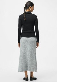 Top negro de manga larga con textura acanalada combinado con una falda larga de color gris claro. El conjunto tiene un diseño sin costuras y se lleva con zapatos planos negros.