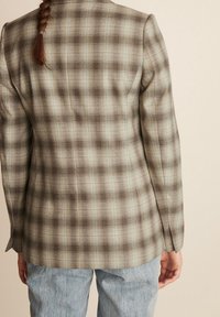 Marynarka w kraty w stonowanych odcieniach zieleni i brązu, charakteryzująca się dopasowanym krojem, gładką fakturą materiału oraz wyrafinowanymi detalami w okolicy ramion.