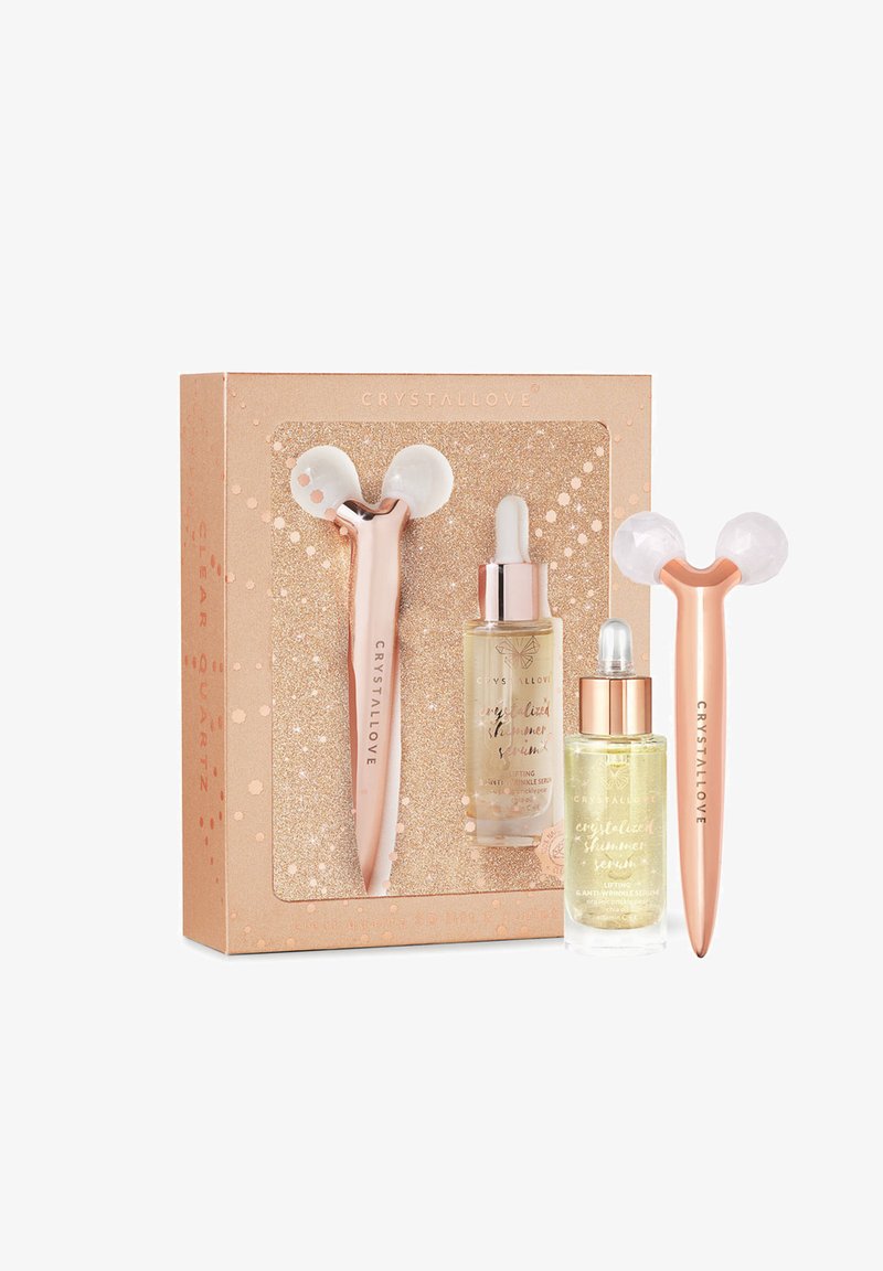 Set aus drei Kristall-Hautpflegewerkzeugen: rosa und roségoldene Jade-Roller, zwei Glas-Tropfer mit schimmernden Seren, verpackt in einer glitzernden Box.
