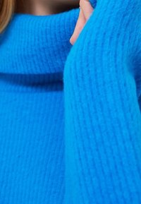 Jasnoniebieski sweter dziany z wysokim, złożonym kołnierzem. Tekstura jest prążkowana, z miękkiej, grubej przędzy dla zapewnienia ciepła.