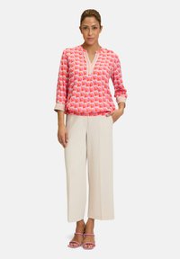 Blusa rosa a fantasia, colorata, con maniche a tre quarti e orlo bianco, abbinata a pantaloni larghi crema e sandali rosa con cinturini.