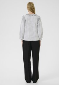 Striped blouse with ruffled shoulders, made of lightweight fabric, paired with black, wide-leg trousers. Soft texture, fitted silhouette.