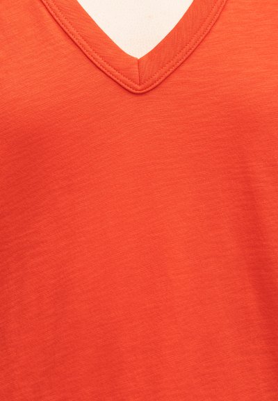 Κοντινή λήψη πορτοκαλί μπλούζας με V-λαιμόκοψη που δείχνει την υφή και τις ραφές.
