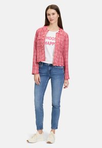 Czerwona i biała tweedowa marynarka o skróconym kroju, zestawiona z białym t-shirtem z napisem "WYBIERZ SZCZĘŚCIE" w różowych literach, niebieskimi jeansami skinny i kremowymi butami.