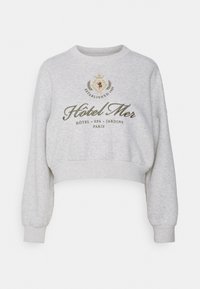 Sweatshirt gris court en molleton. Présente une broderie sur le devant avec "Hôtel Mer" et des détails parisiens, des poignets côtelés et un col rond.