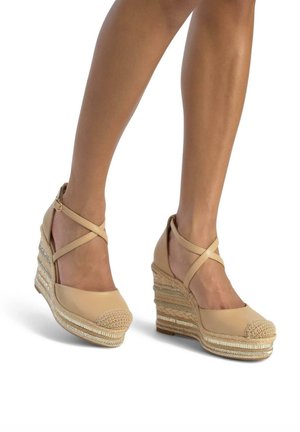 Beige wedge sandals met een getextureerde teenkap, enkelbandjes en een gelaagde jute hak met geweven patronen en metalen accenten.