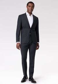 Completo su misura grigio scuro con giacca a un bottone, pantaloni slim-fit e camicia bianca con colletto. Tessuto liscio, design minimalista.