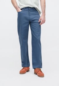 Μπλε παντελόνια με ίσια γραμμή, φτιαγμένα από λείο ύφασμα. Διαθέτουν πλαϊνές τσέπες και κλείσιμο με κουμπί στη μέση. Συνδυάζονται με πορτοκαλί παπούτσια.