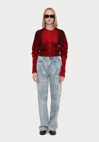 Červený kardigan s dlouhým rukávem, puffovými rameny a zapínáním na knoflíky, v kombinaci se světle modrými džíny s potiskem obličejů a volným střihem.